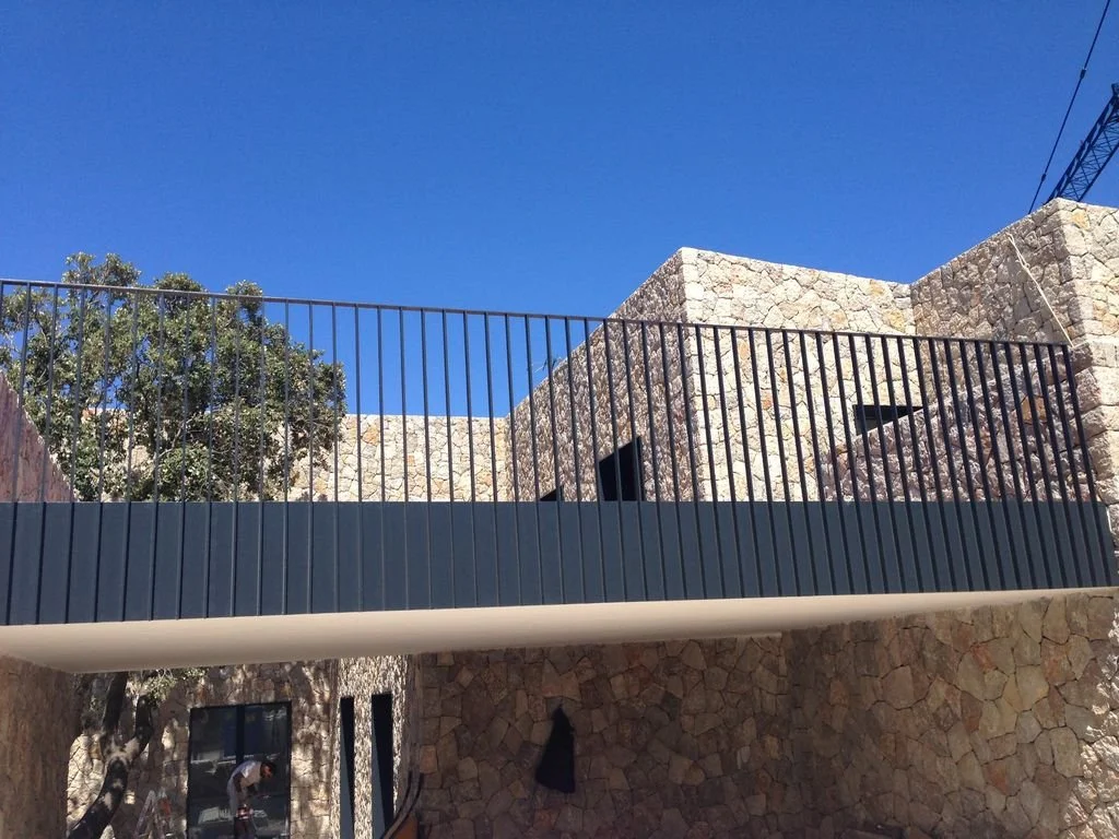 Edificio de piedra con balcón de barandilla de metal y cielo azul en el fondo.