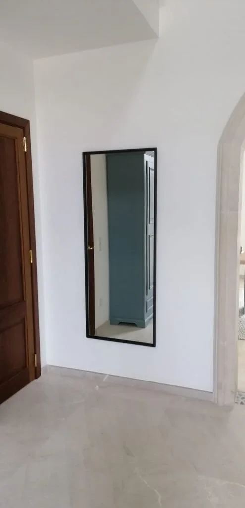 Espejo rectangular colgado en una pared blanca en una habitación interior.