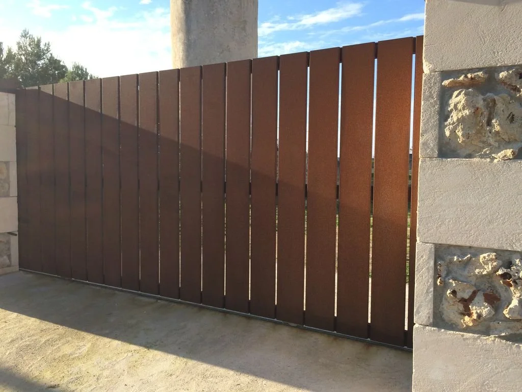 Cerca de madera marrón en un muro de piedra y concreto, con sombra proyectada por la cerca.