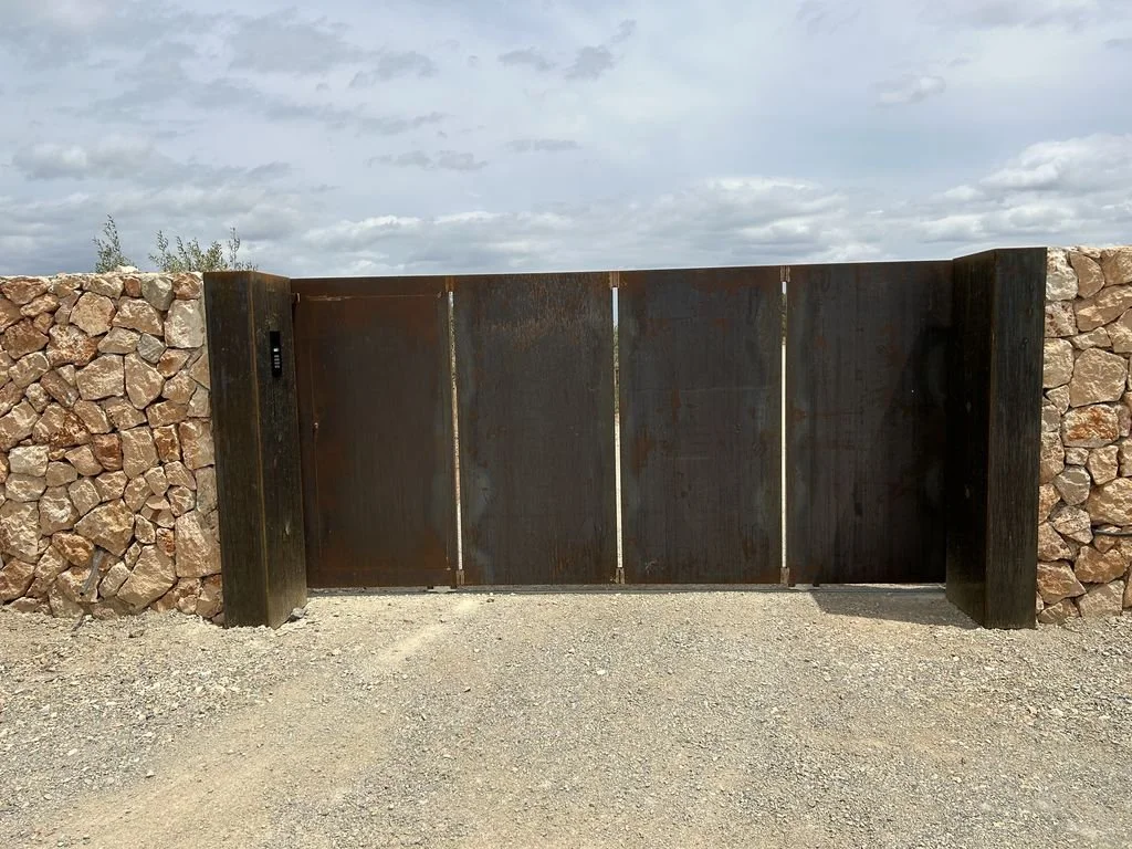Puerta de metal oxidada entre muros de piedra