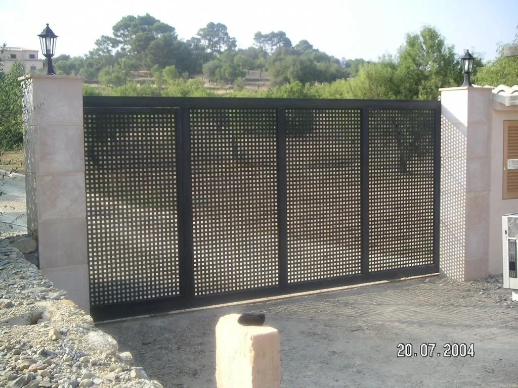 Puerta de metal con patrón de rejilla negra en un muro de piedra, en un entorno al aire libre con árboles y colinas. Fecha de la foto: 20 de julio de 2004.
