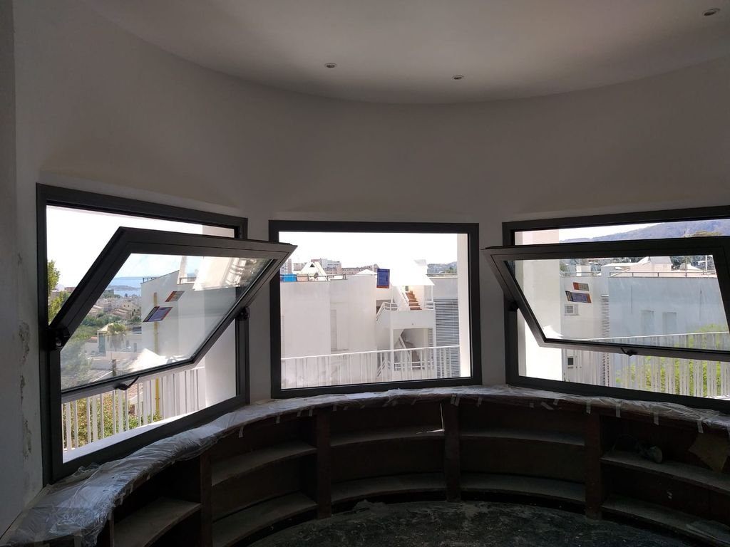 Vista desde el interior de una casa en construcción con ventanas abiertas y vista a edificios y montañas en el fondo.
