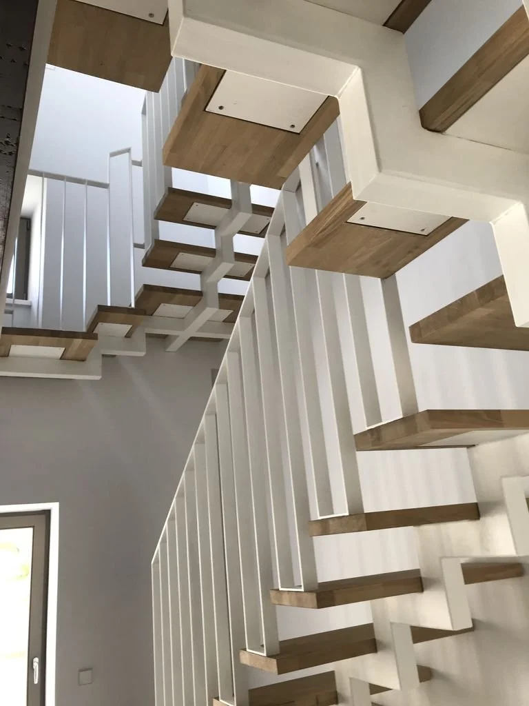 Escaleras modernas de madera con barandillas blancas, vistas desde abajo hacia arriba en un interior de casa con paredes blancas.