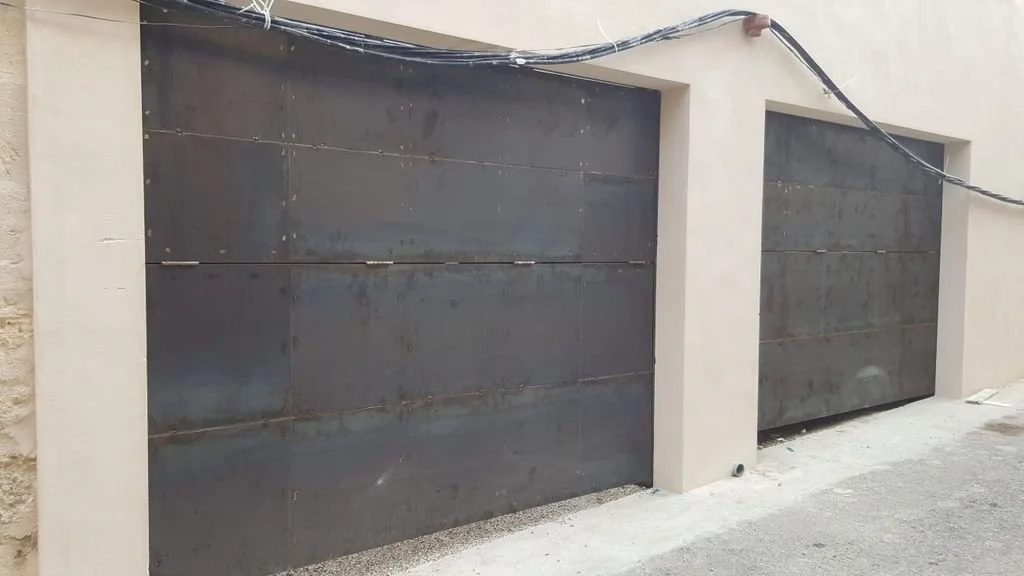 Dos portones metálicos grandes con estructura de cemento en un muro de construcción.
