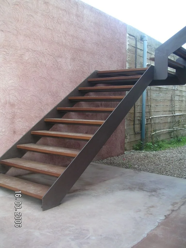 Escalera de metal y madera junto a pared de color rosa y muro de ladrillos.