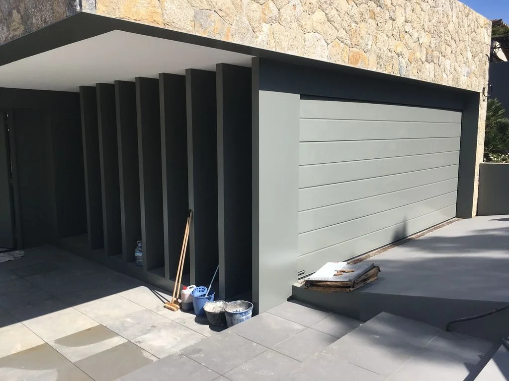 Construcción de una cochera moderna con puertas corredizas grises y paredes de piedra en la parte superior.