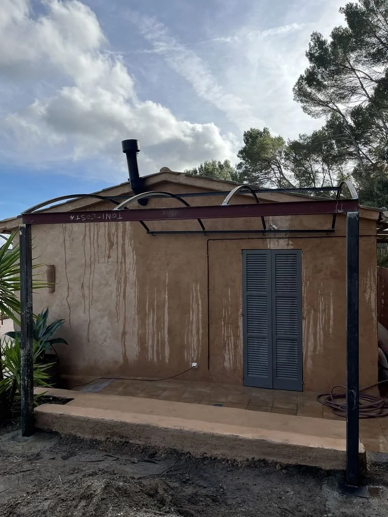 Estructura metálica en construcción frente a una pared con un ventilador y una puerta de cortinas de madera.