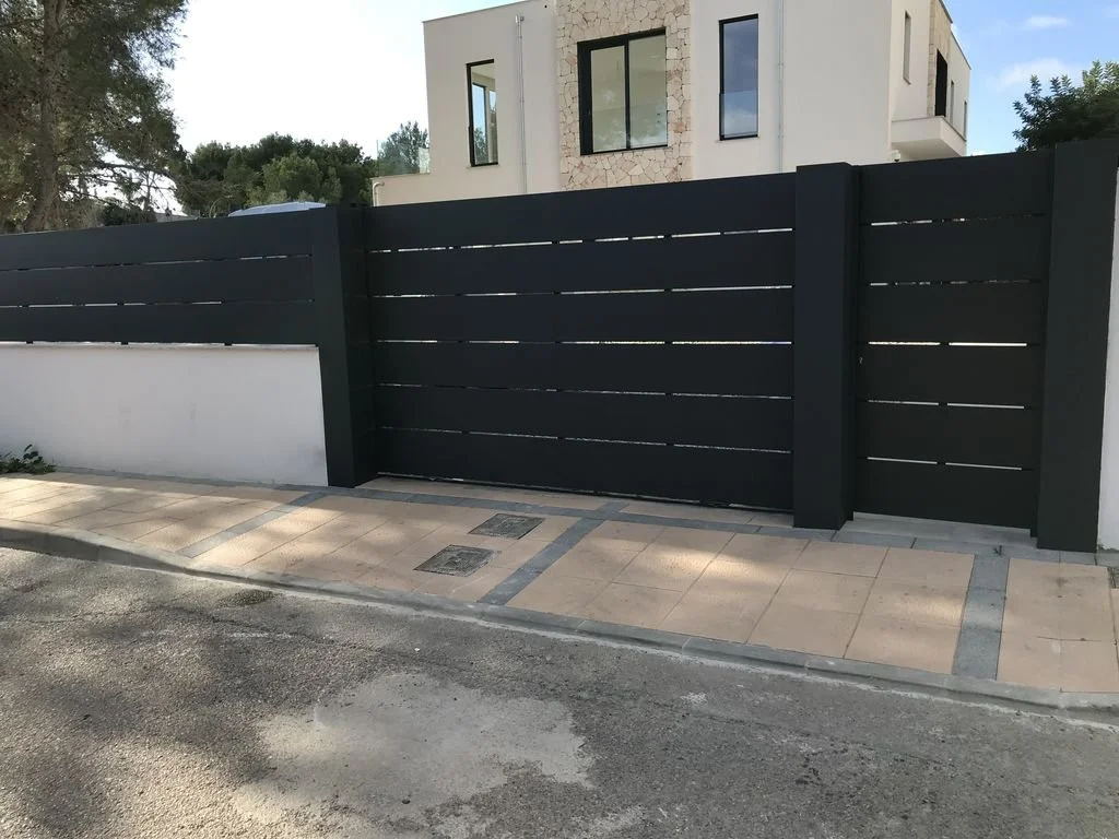 Muro de privacidad negro con puerta de entrada en la entrada de una casa moderna blanca con ventanas grandes.
