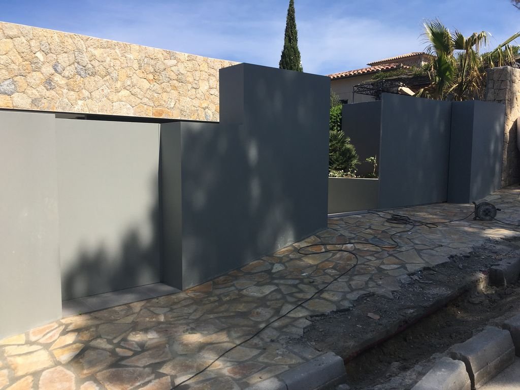 Muro gris en construcción en una calle de piedra, con herramientas eléctricas y cables en el suelo