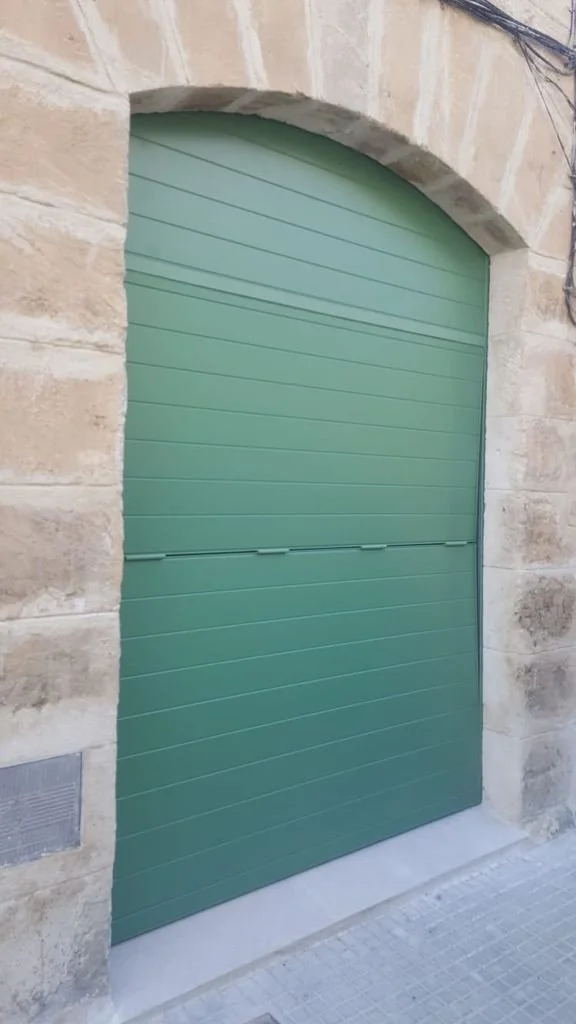 Puerta de garaje de color verde instalada en una fachada de piedra.