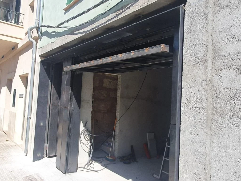 Fachada en construcción con estructura metálica y paredes de cemento, sin puerta instalada y con cables expuestos.
