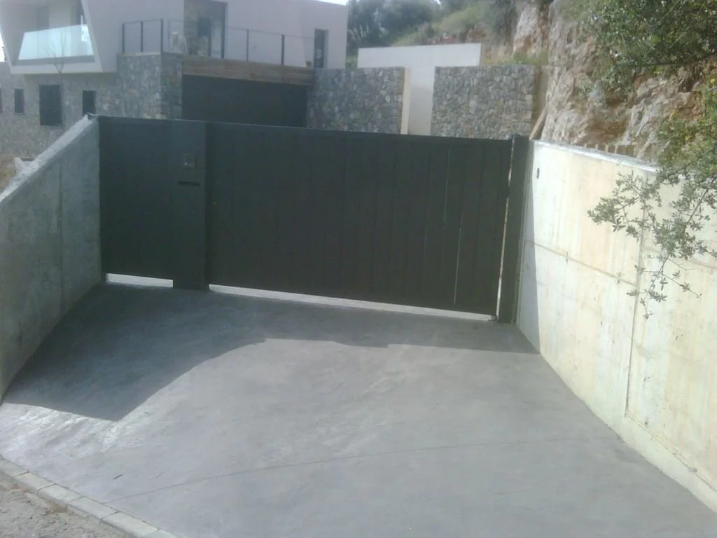 Entrada de garaje con una puerta negra en un entorno residencial moderno con paredes de piedra y concreto.