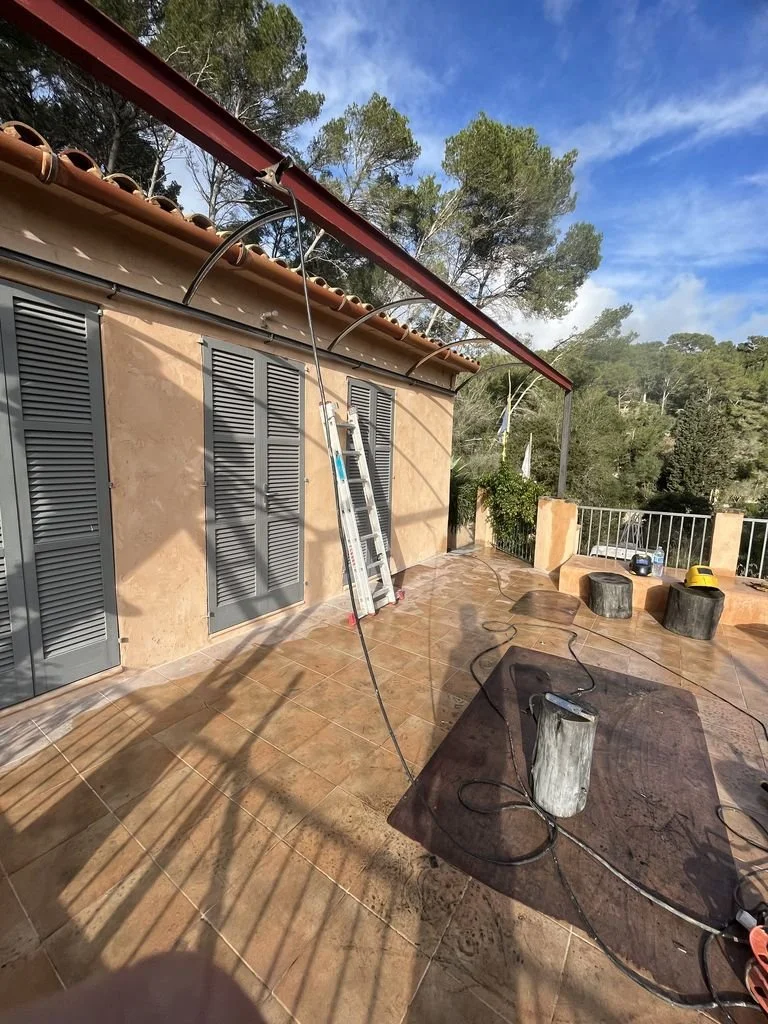 Área en una terraza exterior en construcción o mantenimiento, con escaleras, cables y herramientas, árboles y cielo azul en el fondo.