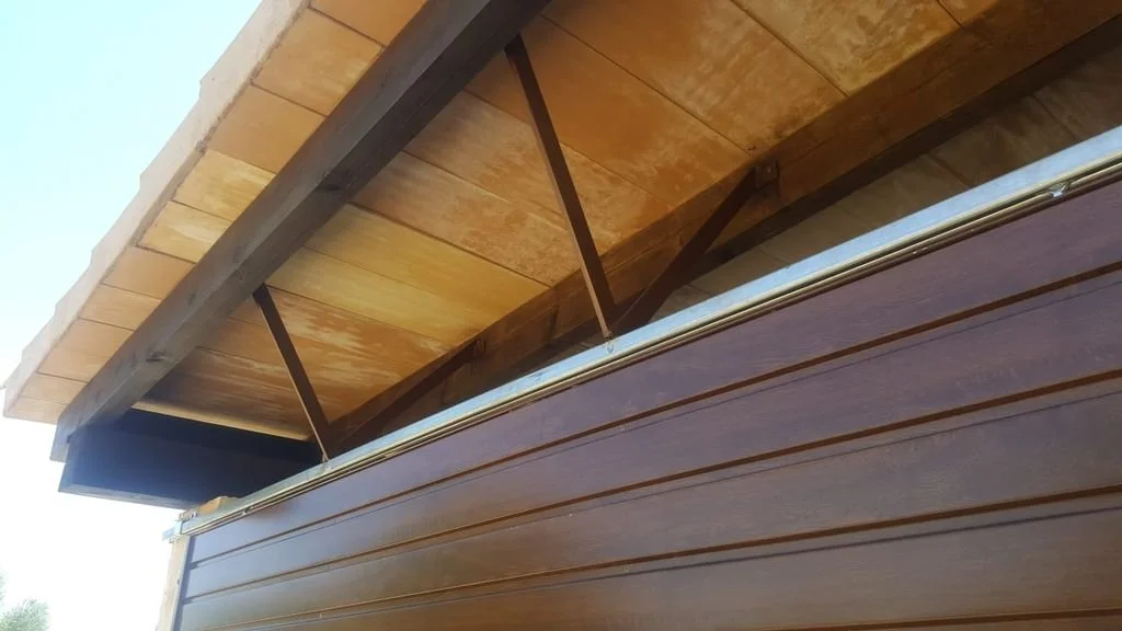 Vista desde abajo de un alero de madera sobre una casa, con tejas de madera.