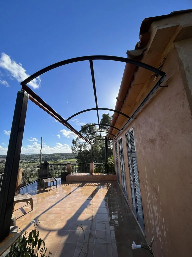 Terraza cubierta con estructura de metal en un edificio, con vista a un paisaje natural bajo un cielo despejado.
