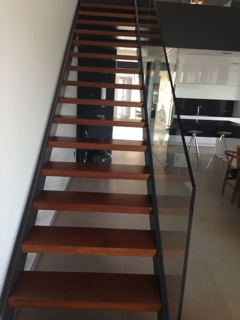 Escalera moderna de madera y metal en el interior de una casa, con barandilla de vidrio.