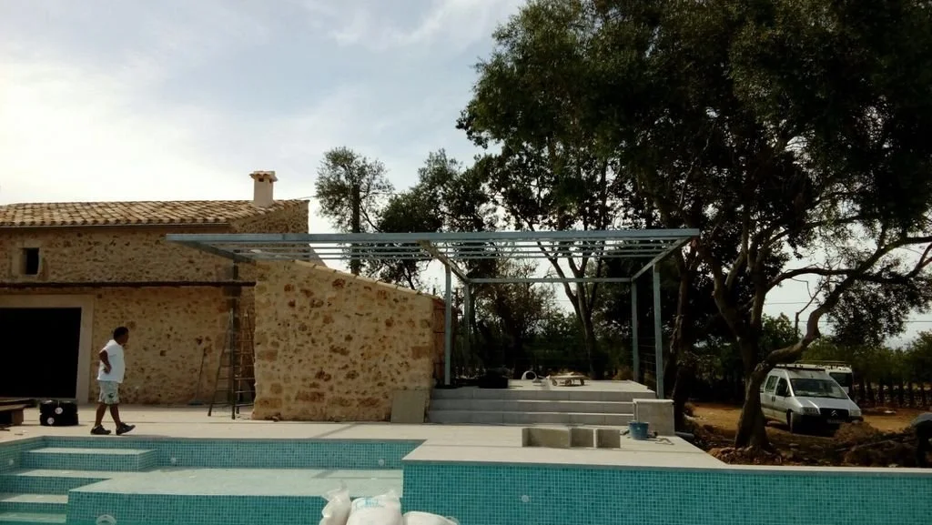 Escalera de piedra, estructura metálica en construcción junto a la piscina y árboles grandes en un patio exterior.