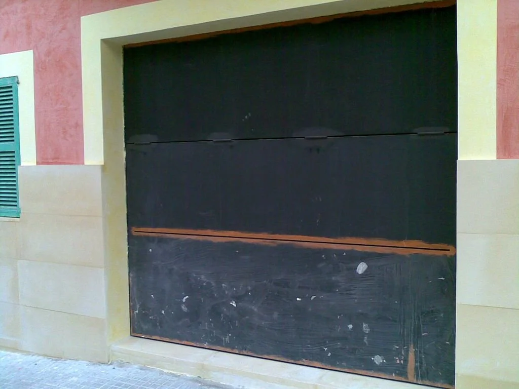 Puerta de garaje en una casa con estructura de paredes de color beige y detalles en tonos rosa y verde