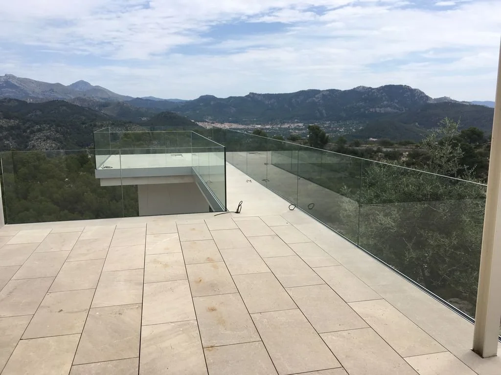 Vista panorámica de montañas y valle desde una terraza con barandilla de cristal en una propiedad moderna.