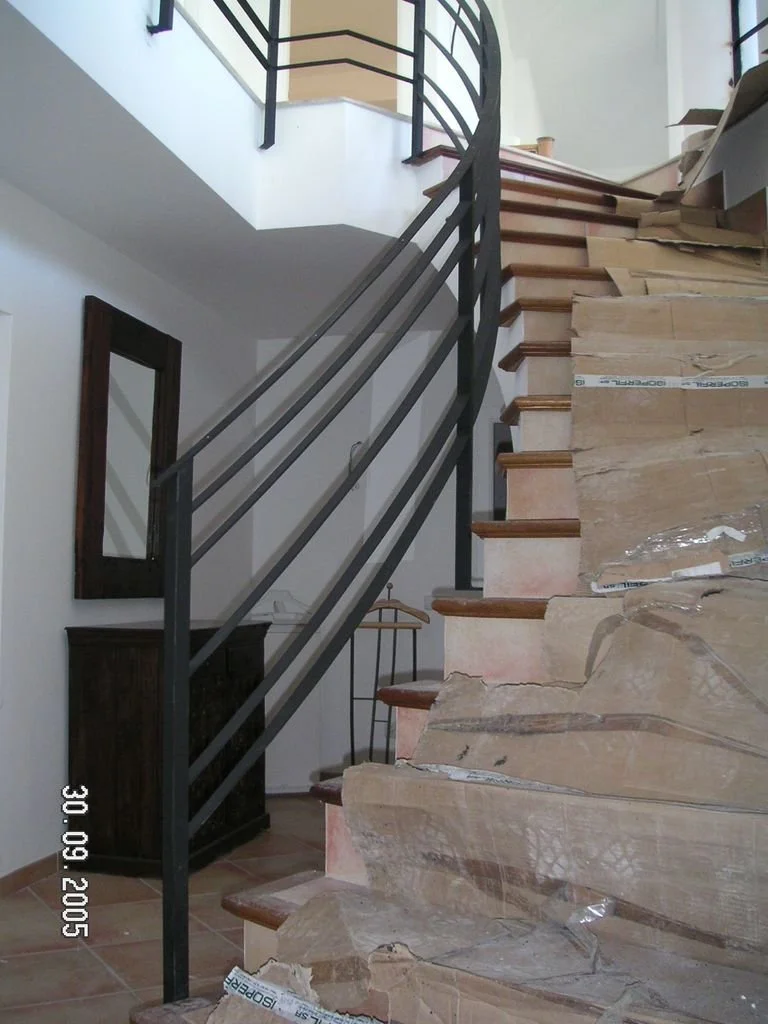 Escaleras en construcción con peldaños de piedra y barandilla de metal, en el interior de una casa.