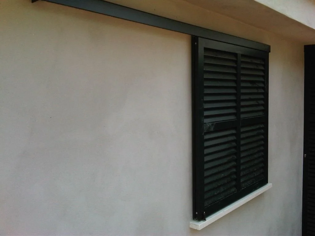 Ventana con persianas negras en una pared blanca de una casa.