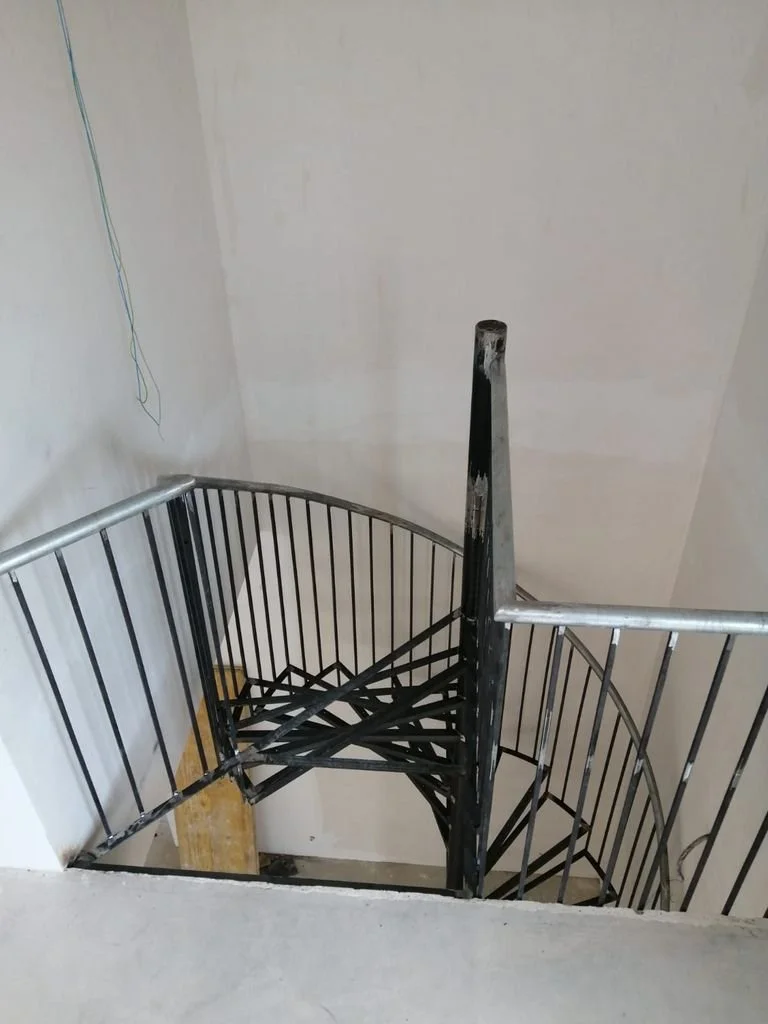 Escalera de caracol en construcción con barrotes de metal y un pasamanos en color plata, en un edificio en construcción.