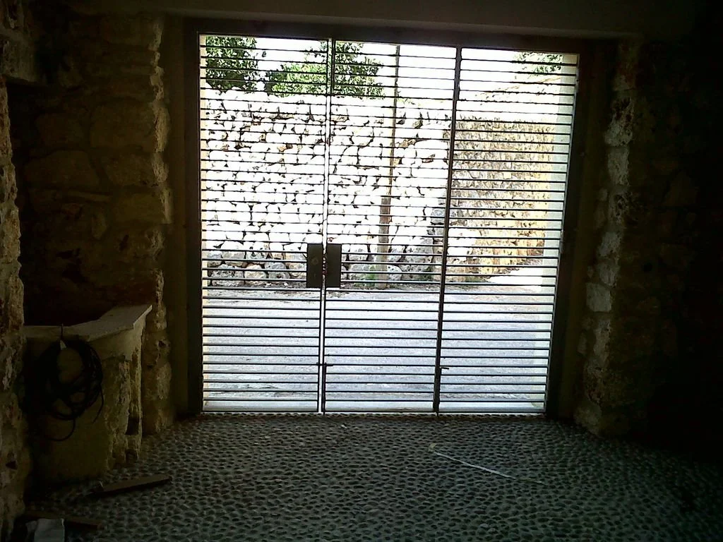 Puerta de metal con rejilla, vista de un muro de piedra y un camino exterior