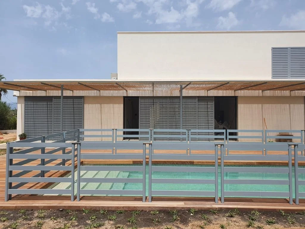 Casa moderna con piscina y terraza de madera, barandales grises y ventanas con persianas.