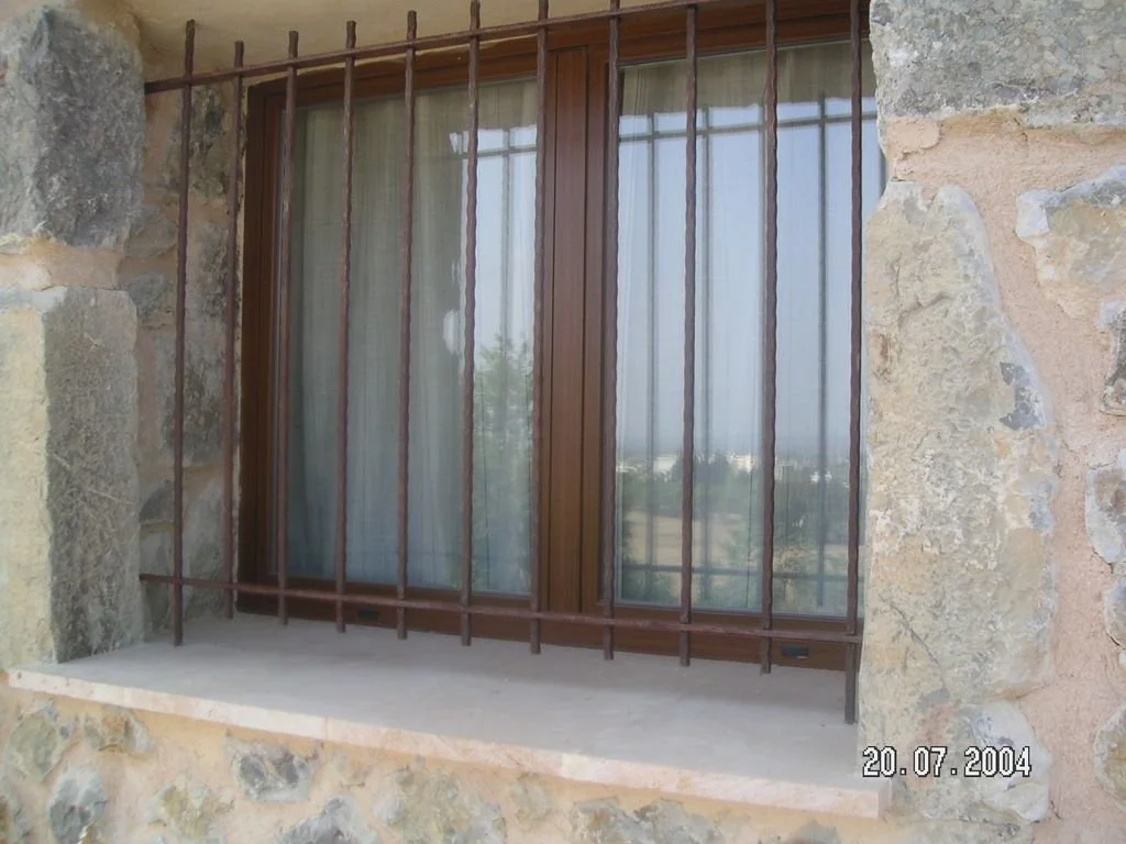 Ventana de cristal con reja de hierro en una pared de piedra.