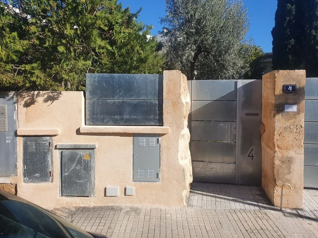 Muro de piedra y metal con puerta y casetas eléctricas.