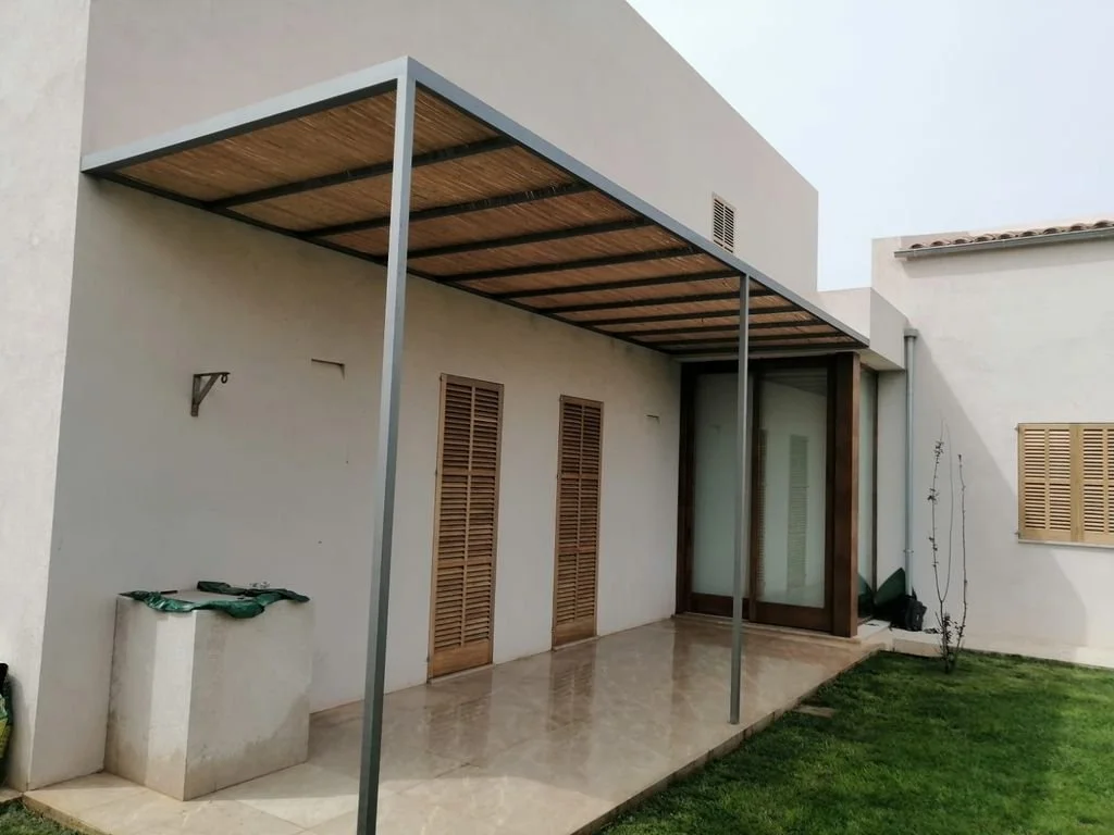 Vista frontal de un patio de casa moderna con una terraza techada y césped.