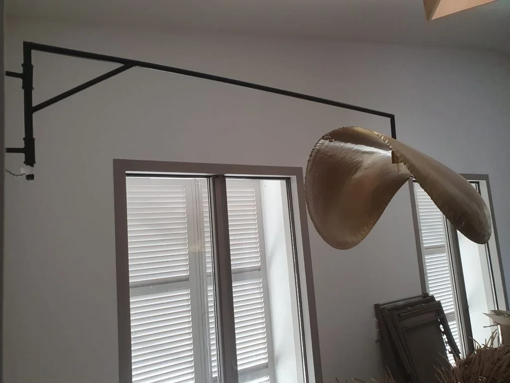 Lámpara de techo dorada en una habitación con ventanas con persianas blancas.