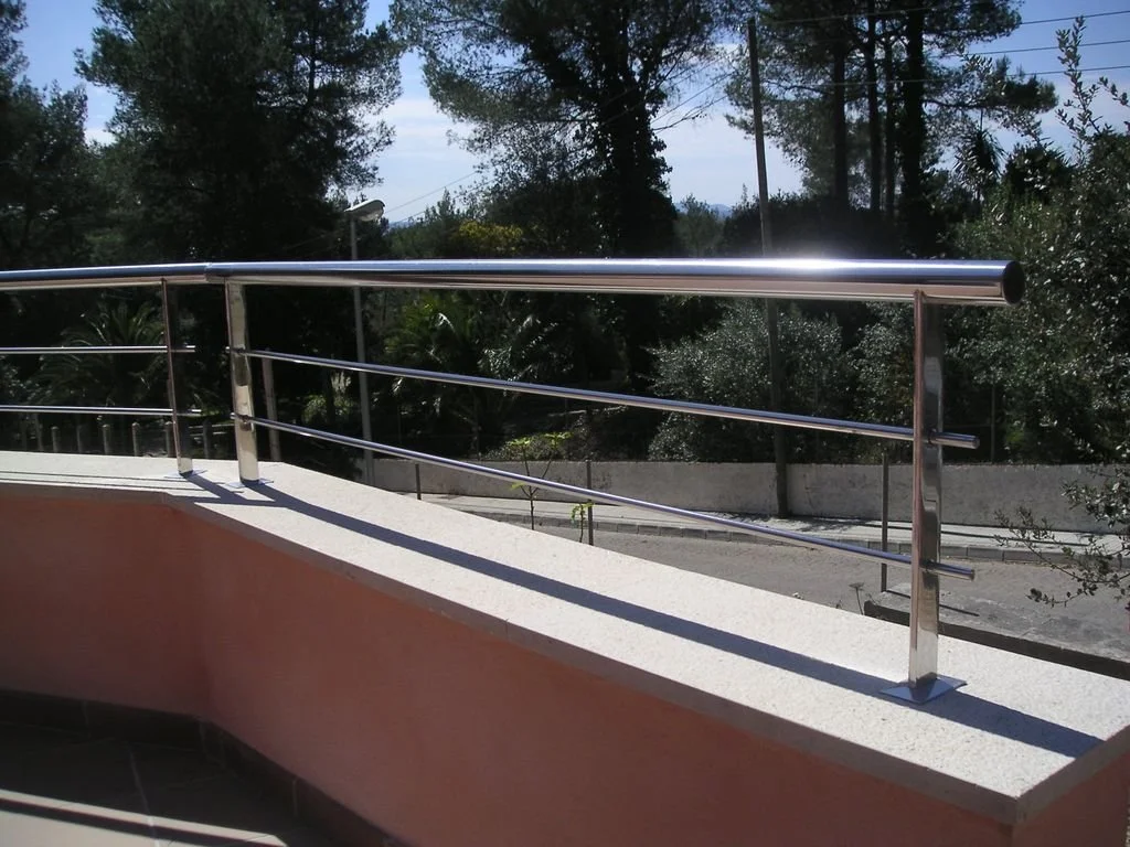 Barandal de metal en una terraza o balcón con vista a árboles y un camino en el fondo.