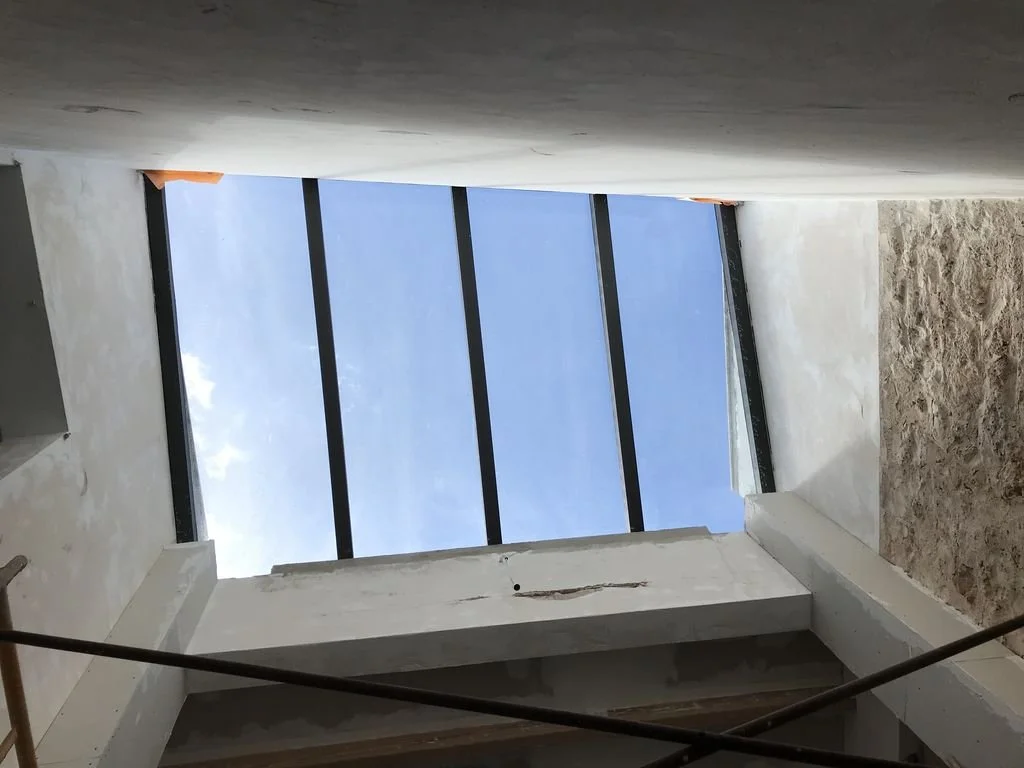 Vista de un espacio en construcción con una ventana de doble acristalamiento, muestra el cielo azul con algunas nubes.