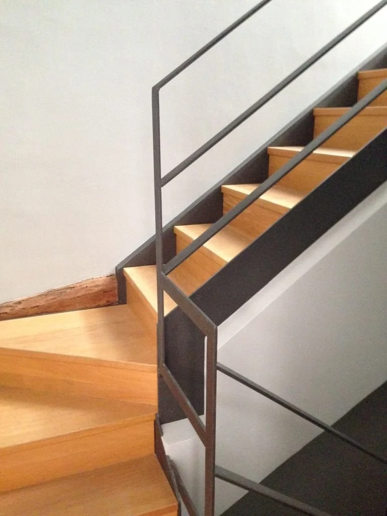 Escalera de madera y metal con barandilla lateral en interiores.