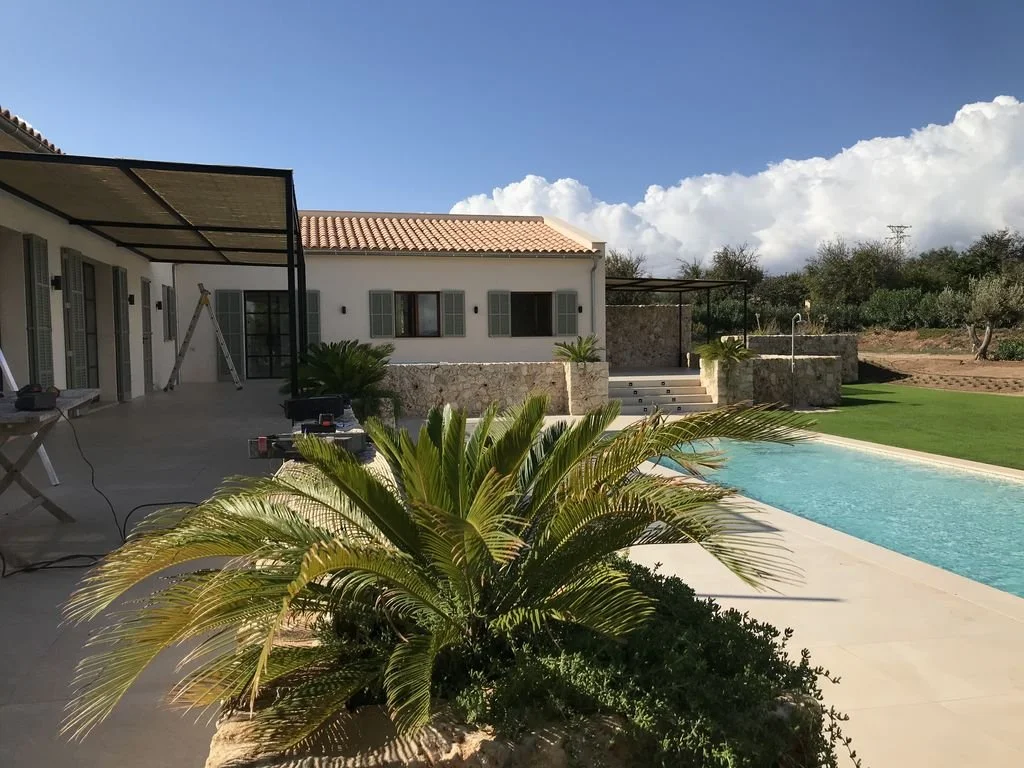Casa moderna con patio, piscina y jardín, día soleado con nubes en el cielo.