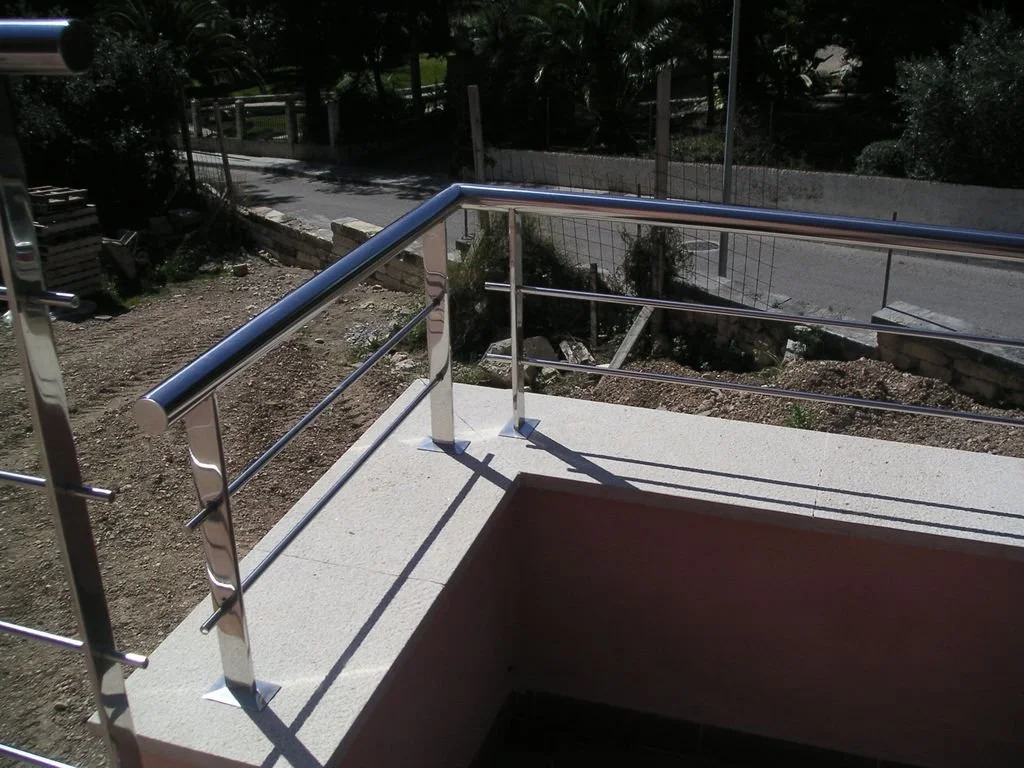 Barandillas de metal en un balcón o terraza con vista a un camino de tierra y vegetación.