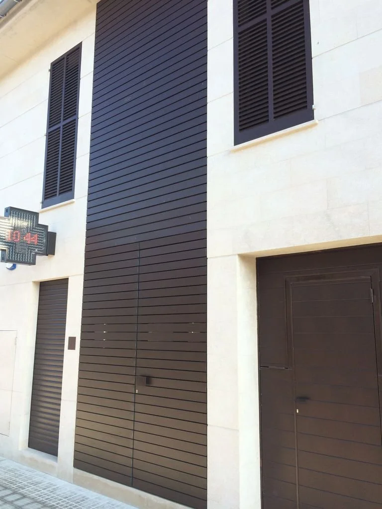 Fachada de edificio con paredes de piedra clara y puertas y ventanas de color negro.