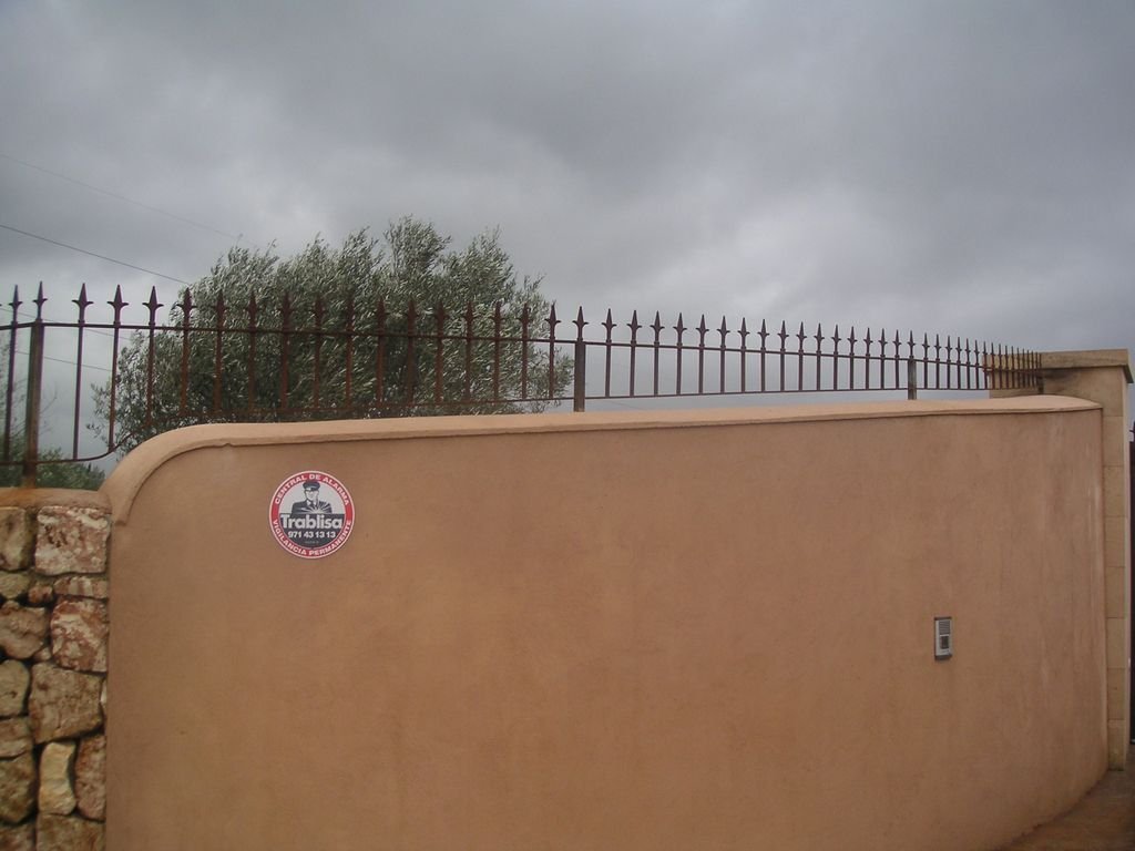 Muro de color beige con una cerca de hierro en la parte superior y un cielo nublado al fondo.