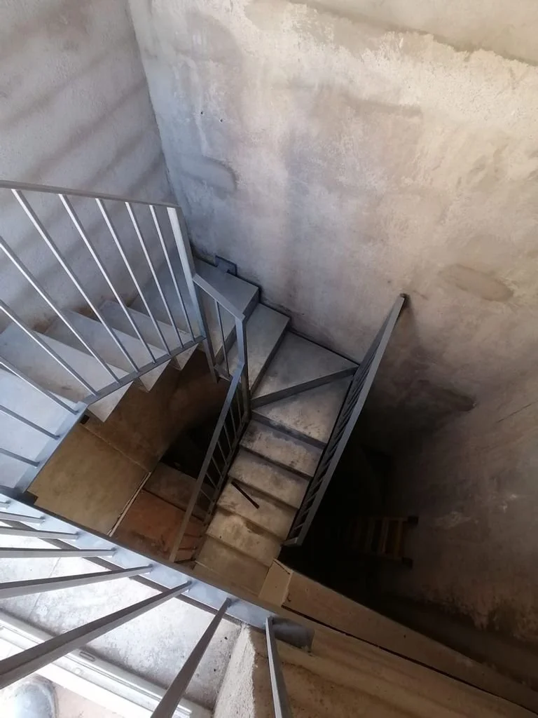 Escaleras de metal en un edificio en construcción o sin terminado, vistas desde arriba hacia abajo, paredes de concreto sin acabados.