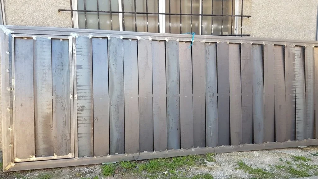 Puerta metálica grande en exterior, con marco de metal, en un entorno urbano.