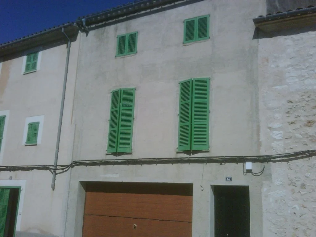 Edificio con paredes de cemento, ventanas con persianas verdes y puerta de garaje de madera.