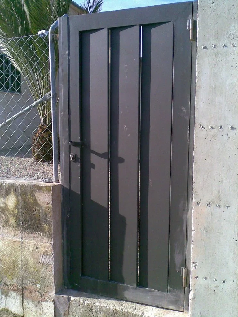 Puerta metálica cerrada instalada en una pared de concreto, con sombra en el suelo