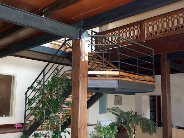 Escalera de metal y madera en interior con plantas y estructura de madera en el techo.