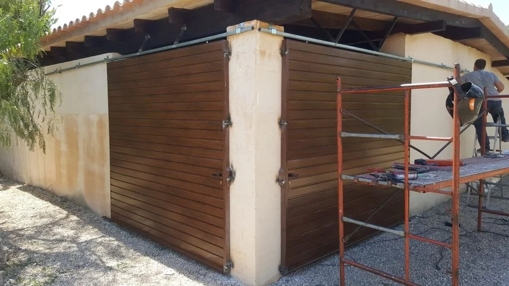 Construcción de puertas de madera enrollables en la esquina de una casa, con una estructura metálica y escaleras.