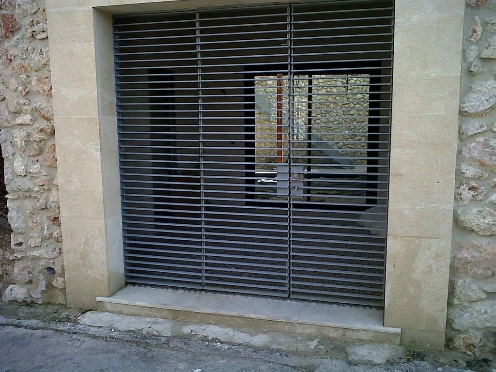 Ventana con rejas negras en un muro de piedra y concreto en una estructura moderna.