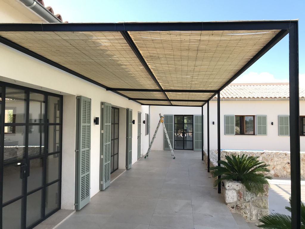 Terraza techada en una casa moderna con ventanas de celosía y plantas ornamentales.