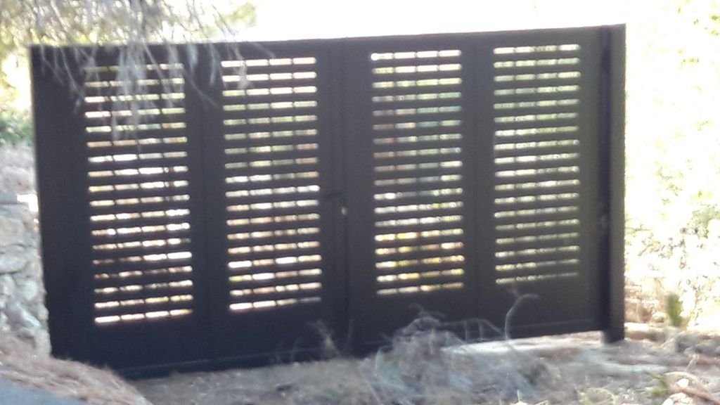 Puerta de madera con una ventana de persianas en un entorno exterior con vegetación y tierra.