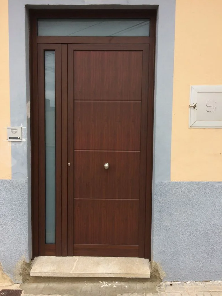Puerta de madera con ventana lateral y grande en una pared de colores pastel, con buzón y buzón de correos al lado.