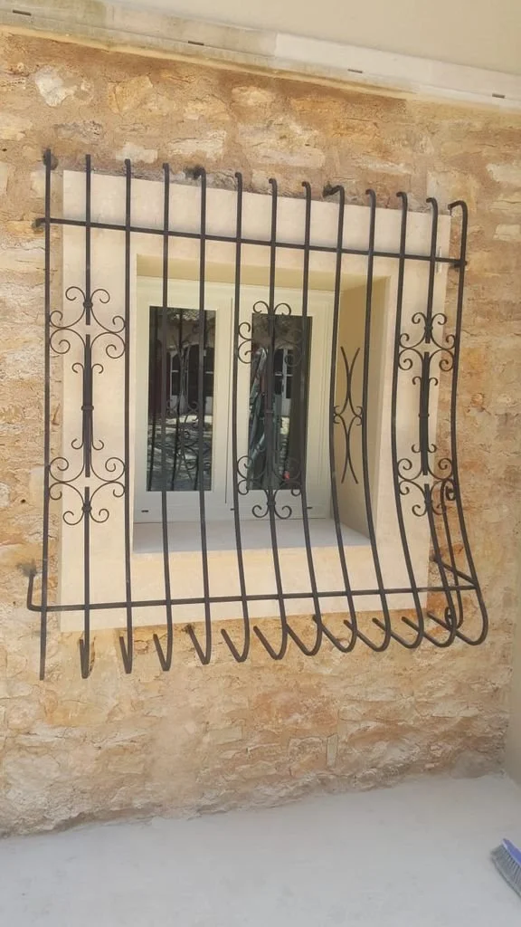 Barra de seguridad de metal en la ventana de una casa con muro de piedra.